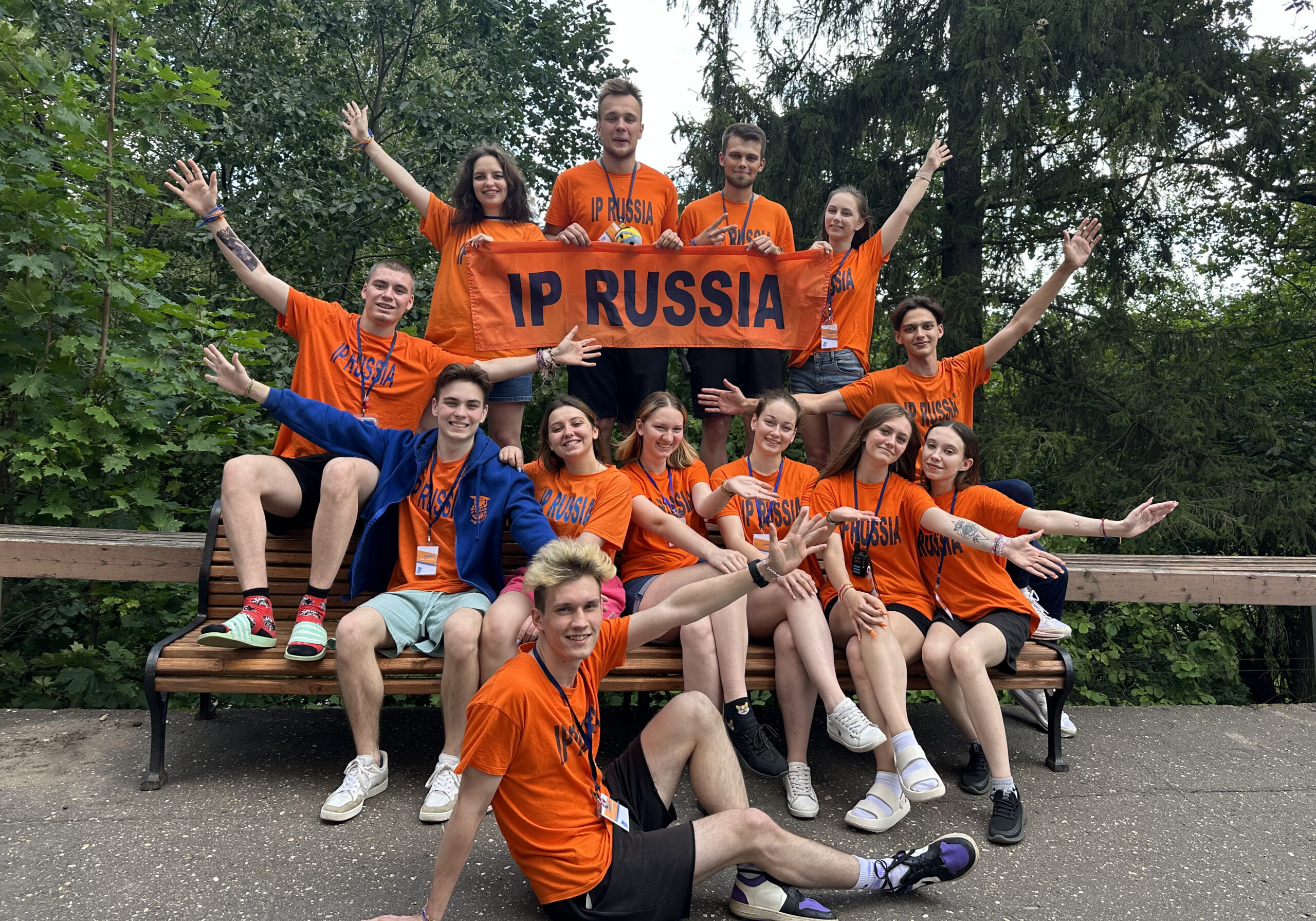 Группа студентов в языковом лагере IP Russia на природе, в оранжевых футболках, держат баннер.