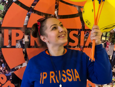Участница языкового лагеря IP Russia с яркими воздушными шарами на фоне логотипа лагеря.