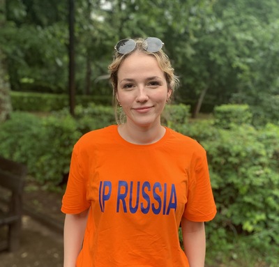 Участница языкового лагеря IP Russia в яркой оранжевой футболке на фоне зелени.